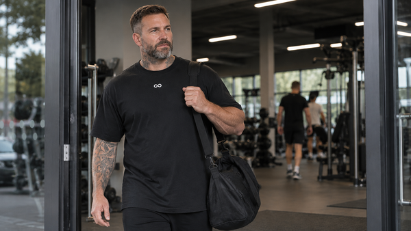 New gym member wearing black LIMITLESS GAINS training apparel walking confidently into a modern gym for their first workout.