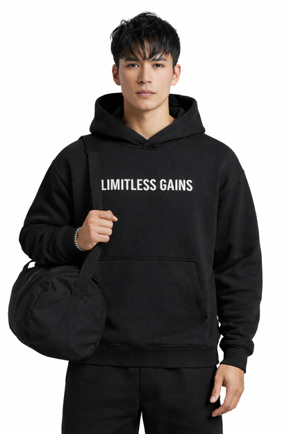 Person wearing a black hoodie with 'LIMITLESS GAINS' text, holding a black duffel bag on a white background
