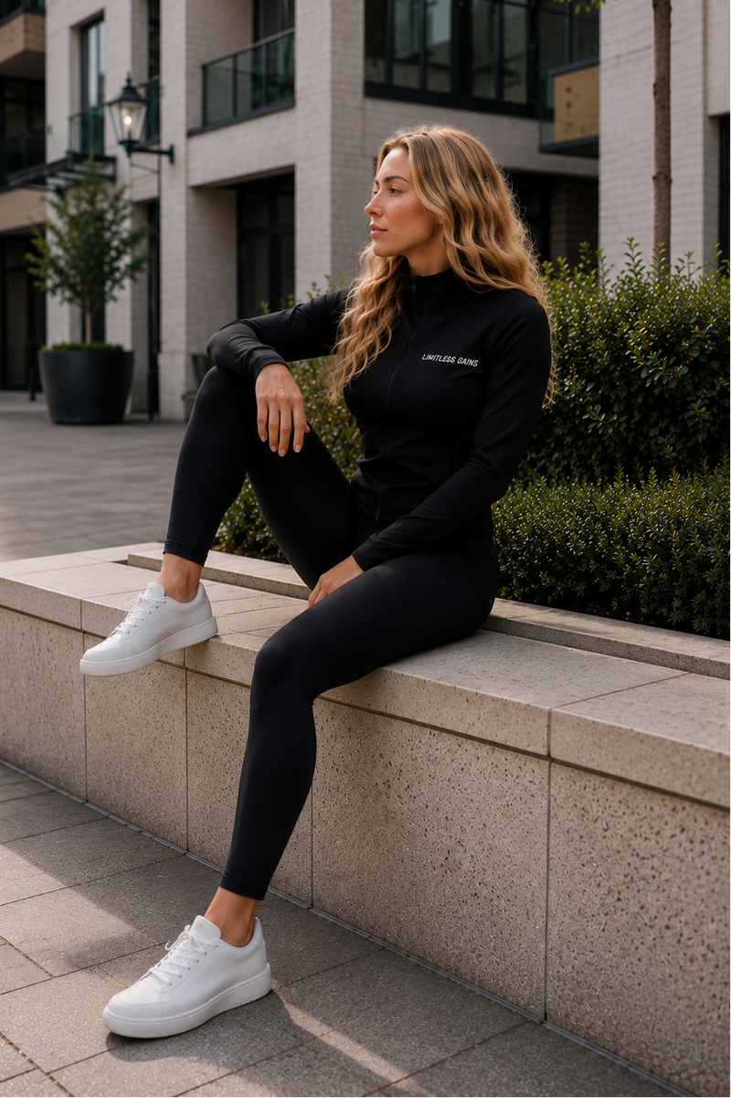 Woman sitting on a ledge wearing black  LIMITLESS GAINS athletic wear with visible branding.