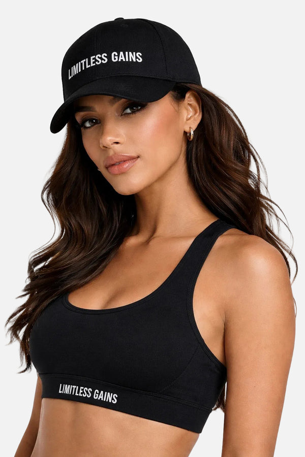 Woman wearing a black sports bra and cap with 'Limitless Gains' text on a white background