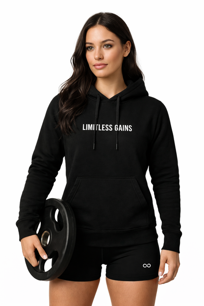 Woman wearing a black 'Limitless Gains' hoodie holding a weight plate on a white background