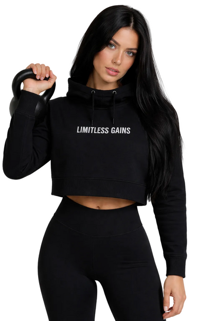 Woman wearing a black hoodie with 'Limitless Gains' text, holding a kettlebell on a white background