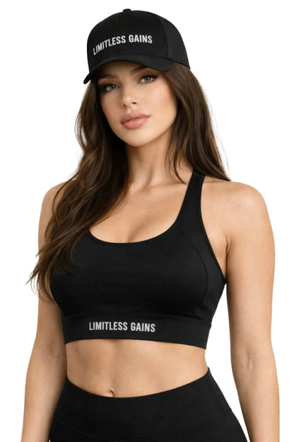 Woman wearing a black sports bra and cap with 'Limitless Gains' branding on a white background
