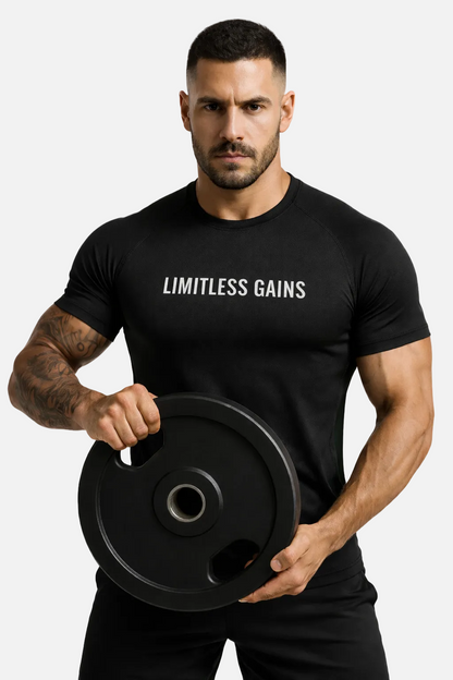 Man wearing a black 'Limitless Gains' t-shirt holding a weight plate on a white background