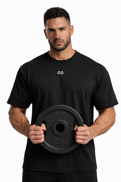 Man holding a black weight plate with a white LIMITLESS GAINS logo on his black t-shirt against a white background