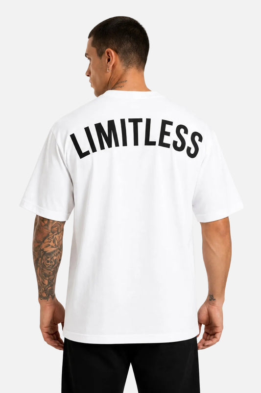 A man viewed from the back wearing a white short-sleeve T-shirt with the word 'LIMITLESS' printed across the upper back in large black letters, paired with black pants against a plain white studio background.